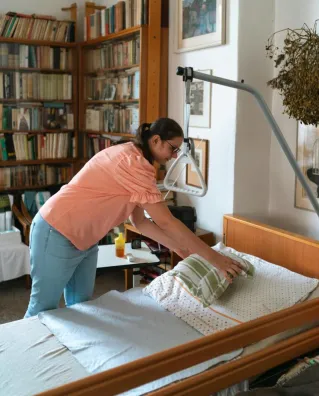 A caregiver adjusts bedding in a cozy home library setting in Prague.