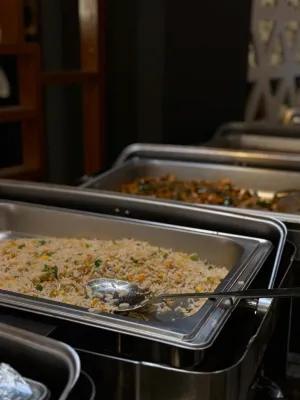A close-up of buffet-style rice and vegetables served in catering trays, ready for guests.