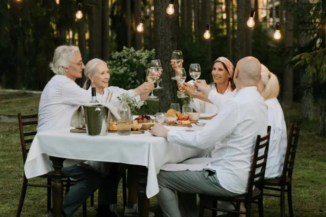 A group of friends toasting in a cheerful outdoor dinner setting surrounded by nature.