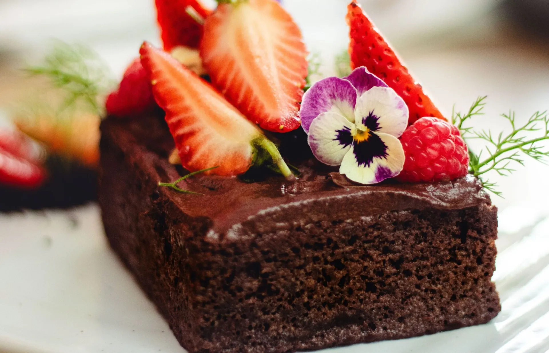 Close-up of a chocolate cake garnished with strawberries, raspberries, and flowers.