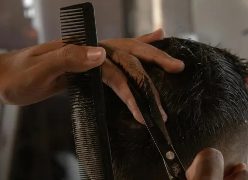 Detailed view of a barber cutting a man's hair with scissors and a comb indoors.