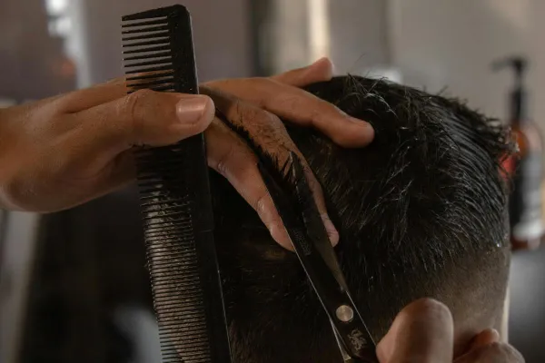 Detailed view of a barber cutting a man's hair with scissors and a comb indoors.