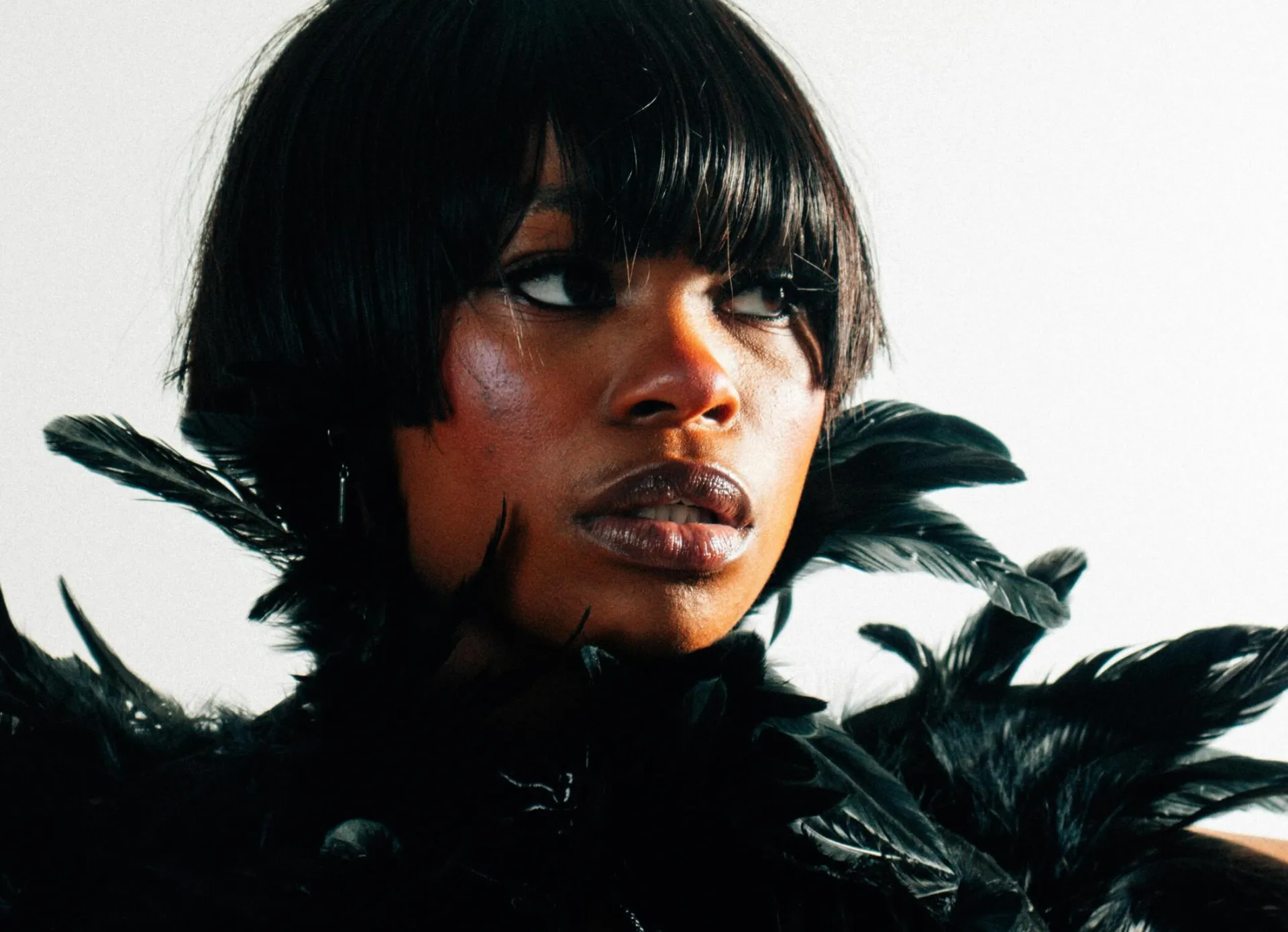 Stunning portrait of a black woman with short hair adorned with feathers, against a white background.