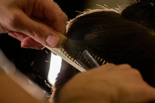 Close-up of a stylist trimming hair with a comb and scissors indoors.