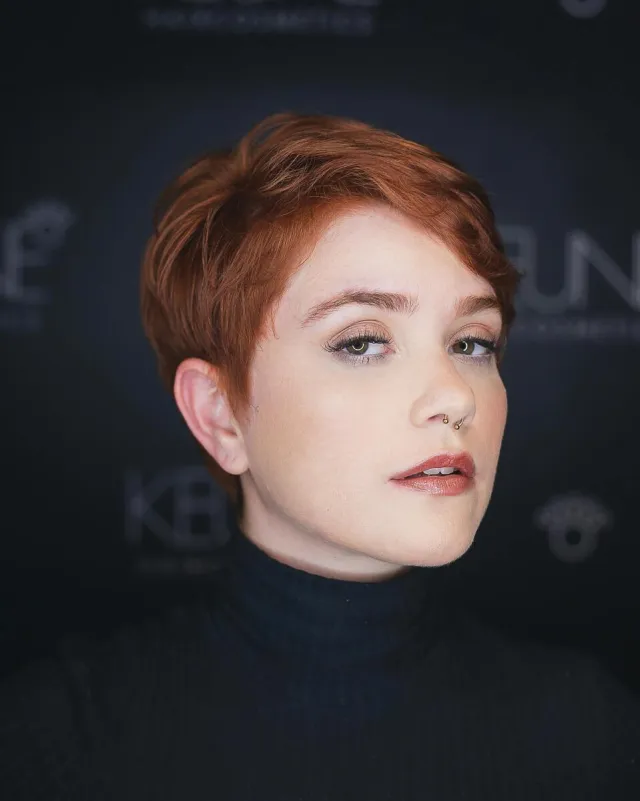 Young ginger female with stylish short haircut and piercing looking at camera on blurred background