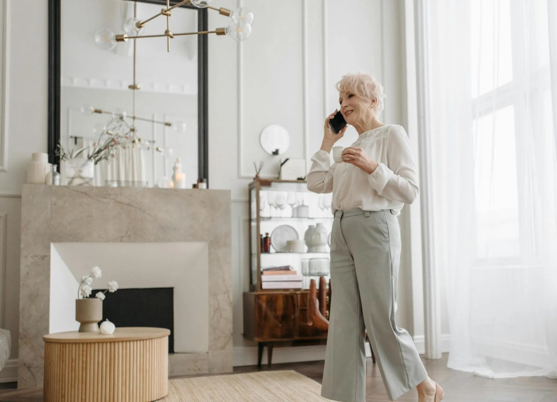 Senior woman with short hair chatting on phone in chic, well-lit living room.