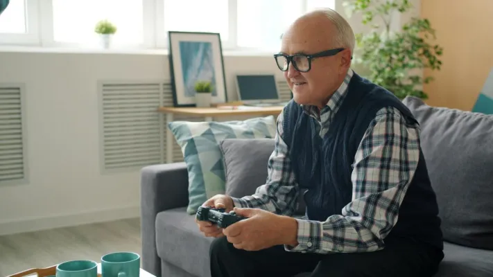 Happy senior man playing video games in cozy living room. Modern lifestyle and leisure activity.