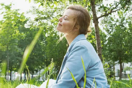 A serene scene of a woman relaxing under a flowering tree in a sunlit park.