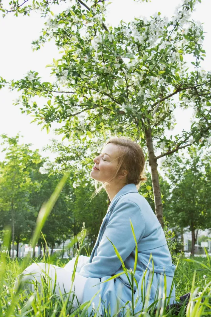 A serene scene of a woman relaxing under a flowering tree in a sunlit park.
