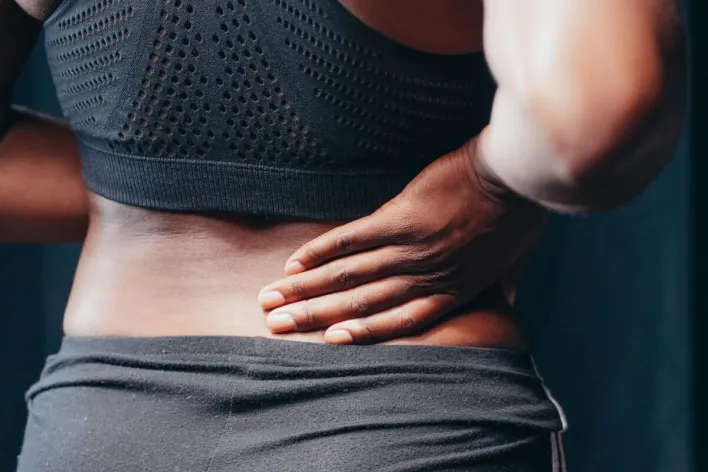 An adult of African descent holding their lower back in pain, indicating discomfort or injury.