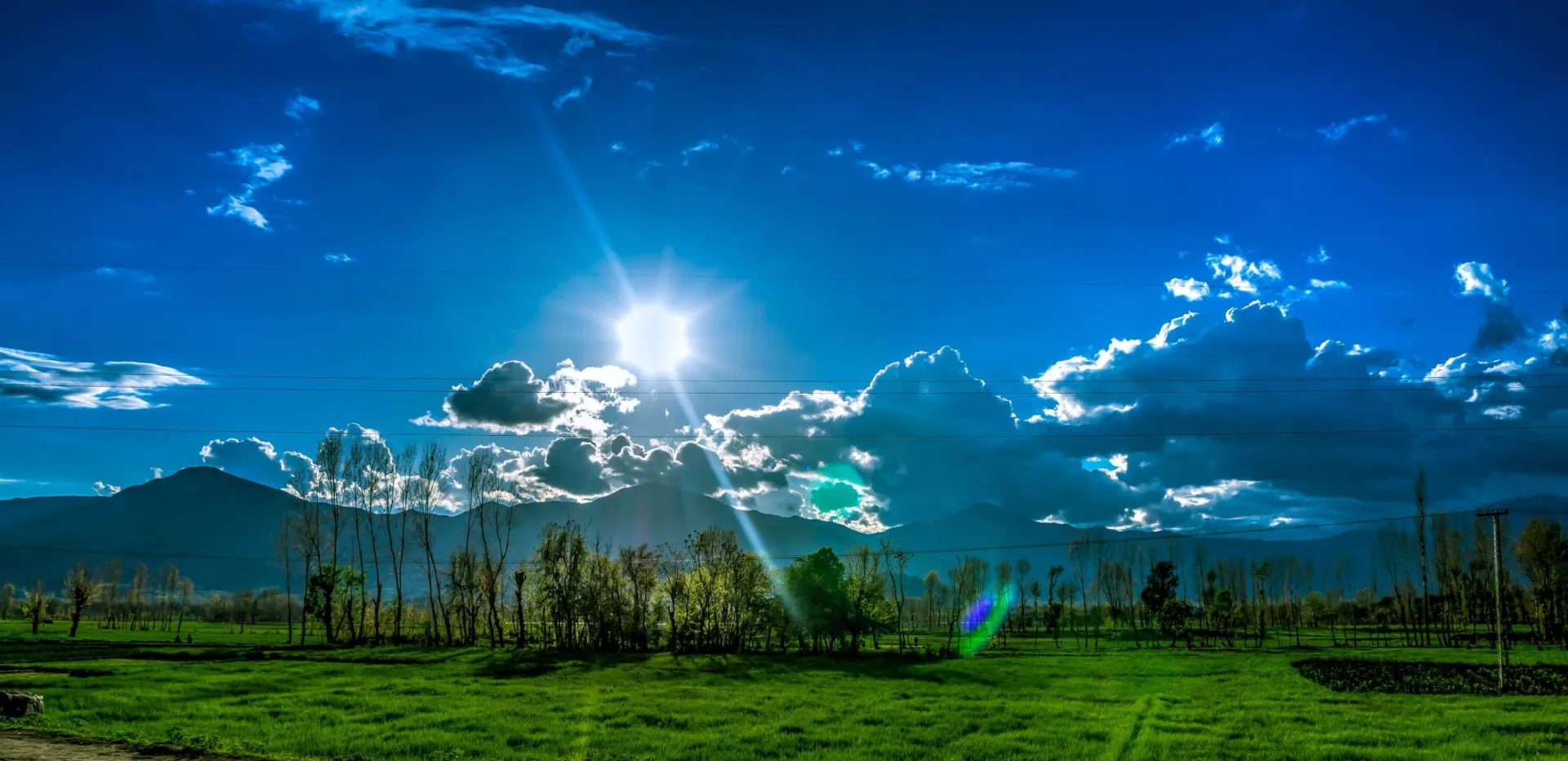 Scenic view of Kalam's green fields and dramatic sky under bright sunlight.