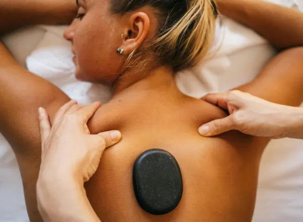 Woman receiving a hot stone massage at a spa, promoting relaxation and wellness.