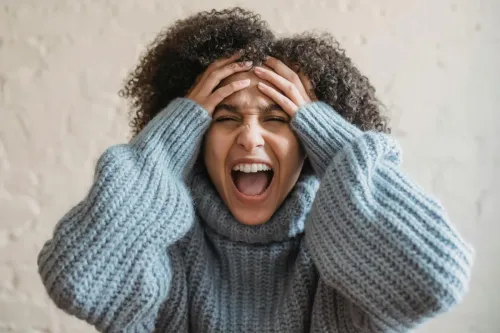 A woman wearing a sweater, expressing frustration with hands on head.