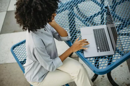 Woman with curly afro hair working on a laptop at an outdoor table, enjoying a relaxed day.