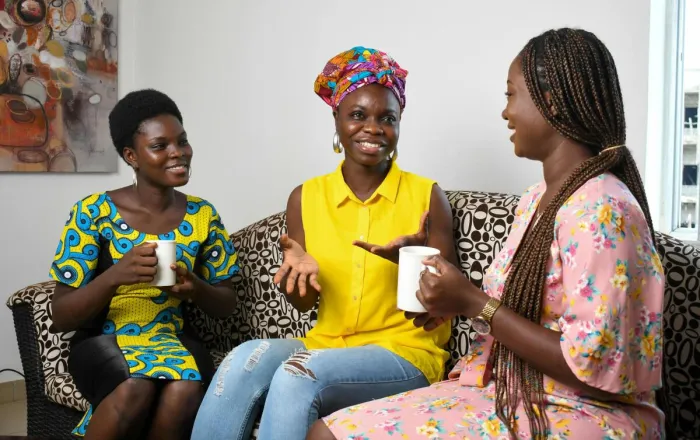 Three women enjoying a casual conversation over coffee in a bright living room.