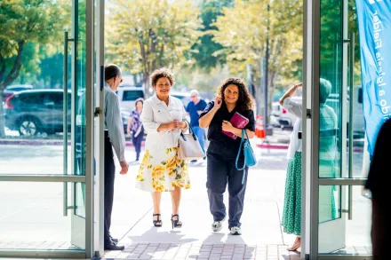 A group of people walking into a building, smiling, on a sunny day.