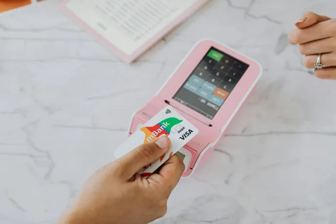 Hand using a contactless card on a pink POS terminal for a wireless transaction.