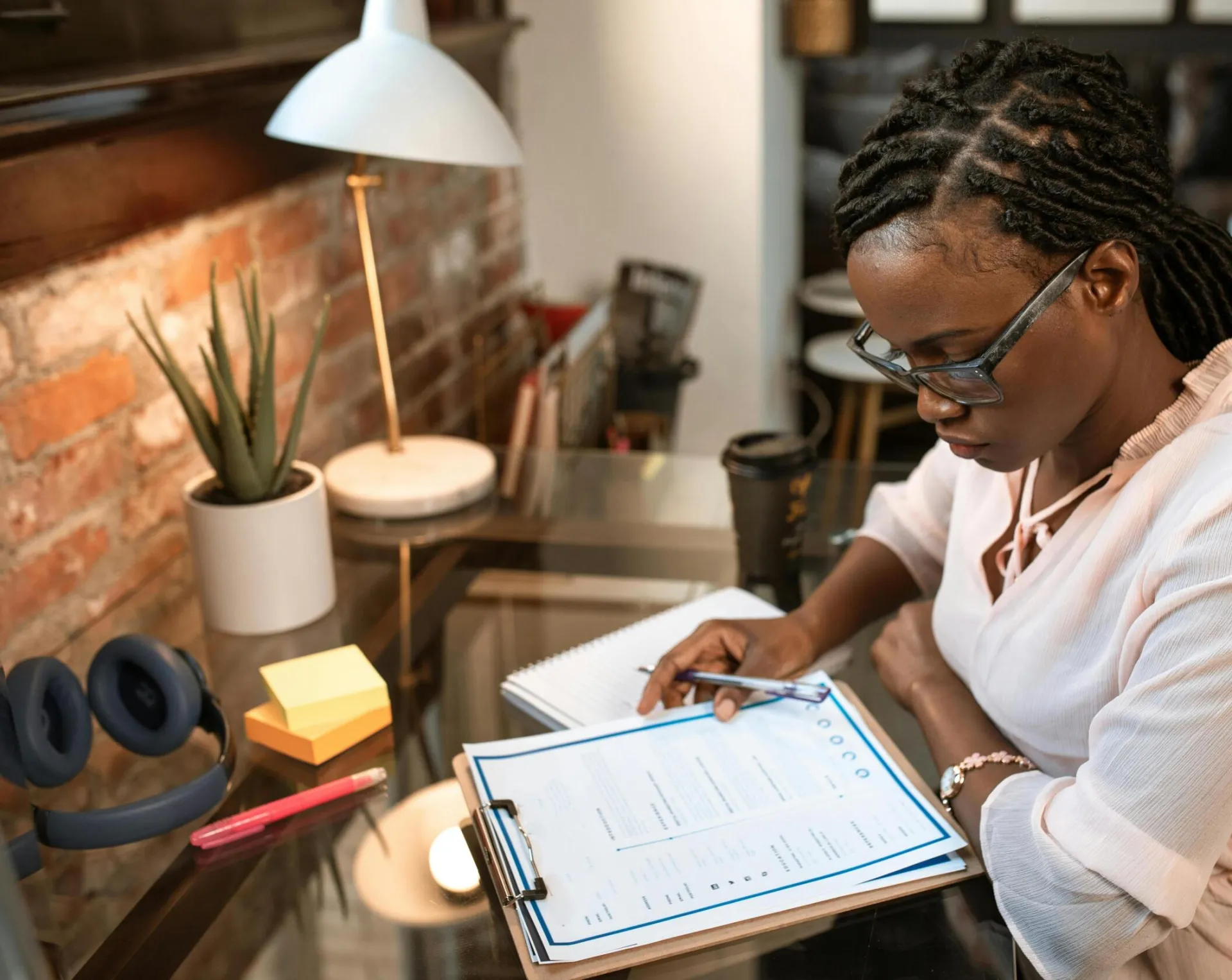 Businesswoman concentrating on paperwork at her office desk, wearing eyeglasses and seated indoors.