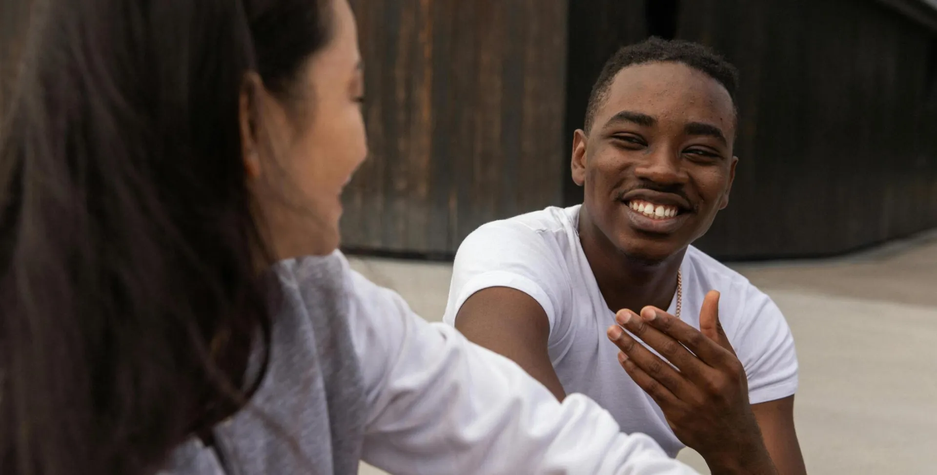 Cheerful young African American guy in casual clothes smiling while chilling on street with crop Asian female friend