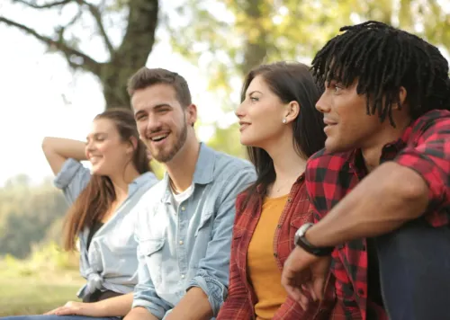 A diverse group of friends laughing and enjoying a sunny day in a park.