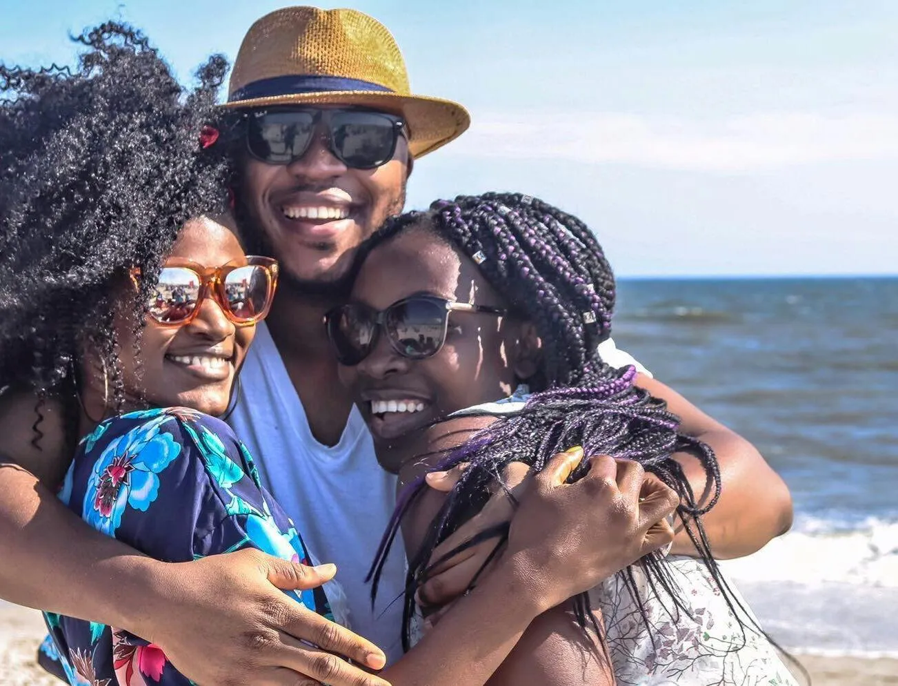 Three friends enjoying a sunny day at the beach, embracing with smiles.