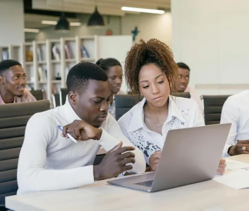 A diverse group of colleagues brainstorming together at a modern office setting with laptops.