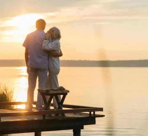 A senior couple embraces on a wooden dock at sunset, exuding tranquility and affection.