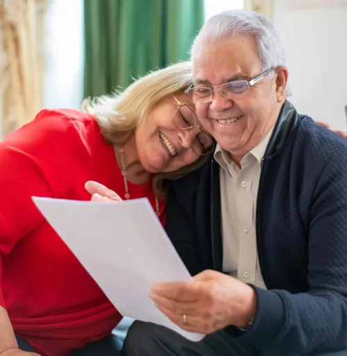 Elderly couple smiling together while looking at a document, showcasing love and happiness indoors.