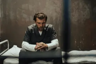 A solitary prisoner in deep thought, sitting on a cell bed inside a prison.