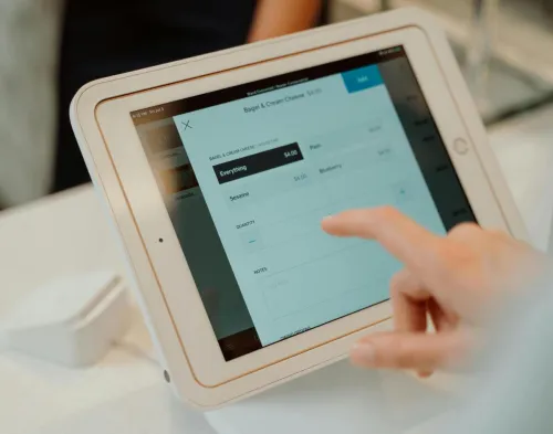 A person uses a tablet-based point-of-sale system by selecting options on a touchscreen device.