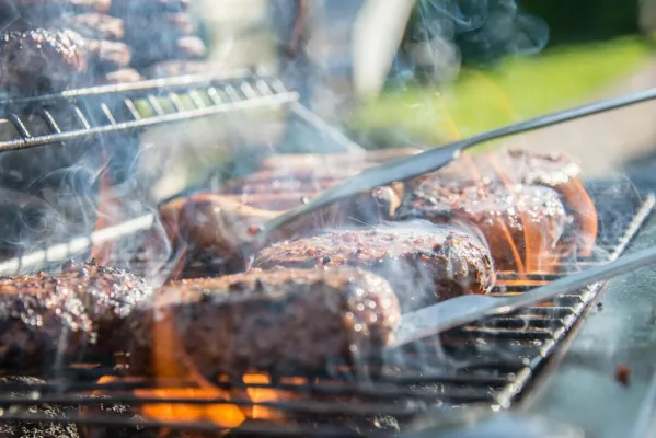 Close-up of sizzling beef burgers on a charcoal grill with flames and smoke.