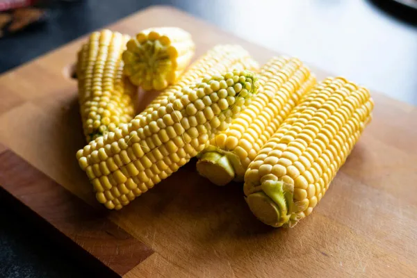 A detailed image of freshly harvested corn cobs placed on a wooden chopping board.