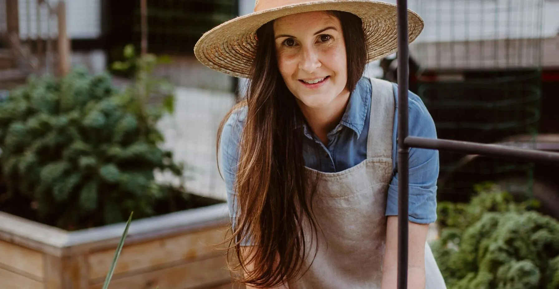 Woman in sun hat gardening in backyard with flowers and vegetables on a sunny day.