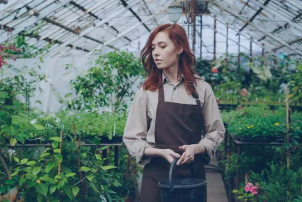 Young female gardener with red hair tending plants in a greenhouse.