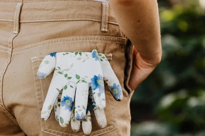 A close-up of floral gardening gloves tucked in the back pocket of outdoor overalls.