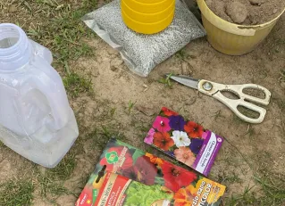 Items for gardening including seeds, scissors, and water container on grass.