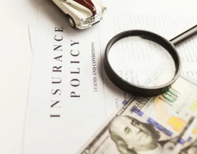 Close-up image of an insurance policy with a magnifying glass, money, and toy car.