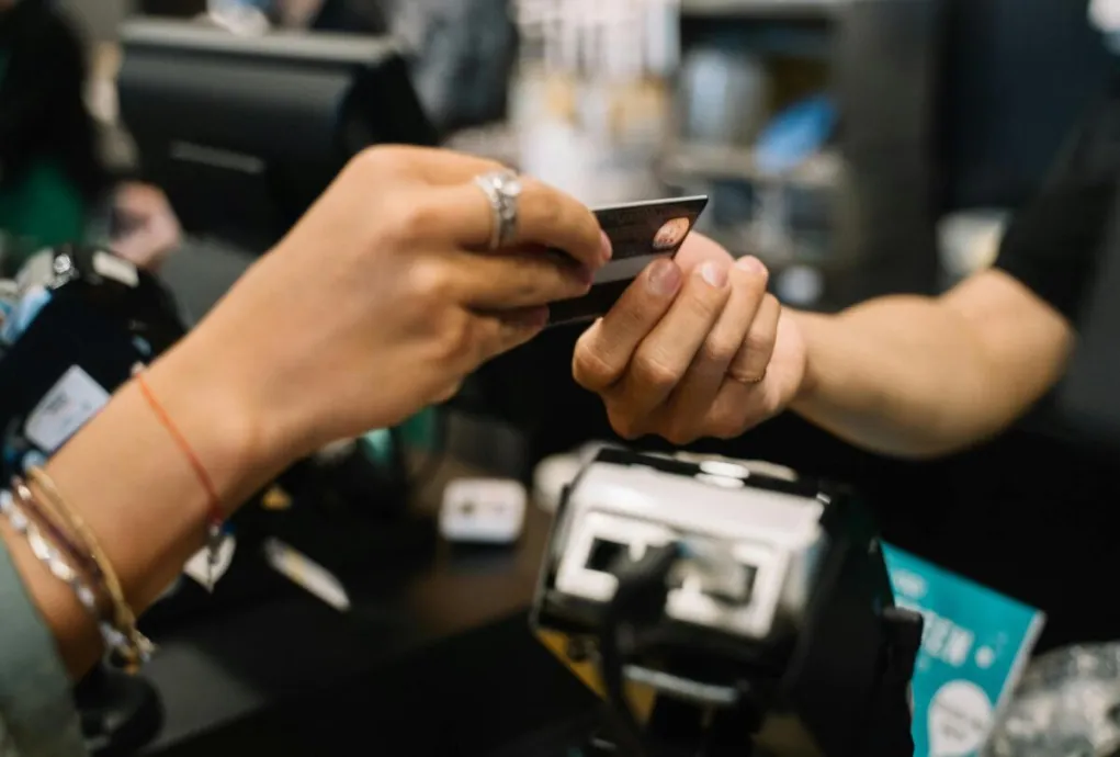 Close-up of hands completing a payment transaction at a retail checkout using a bank card.