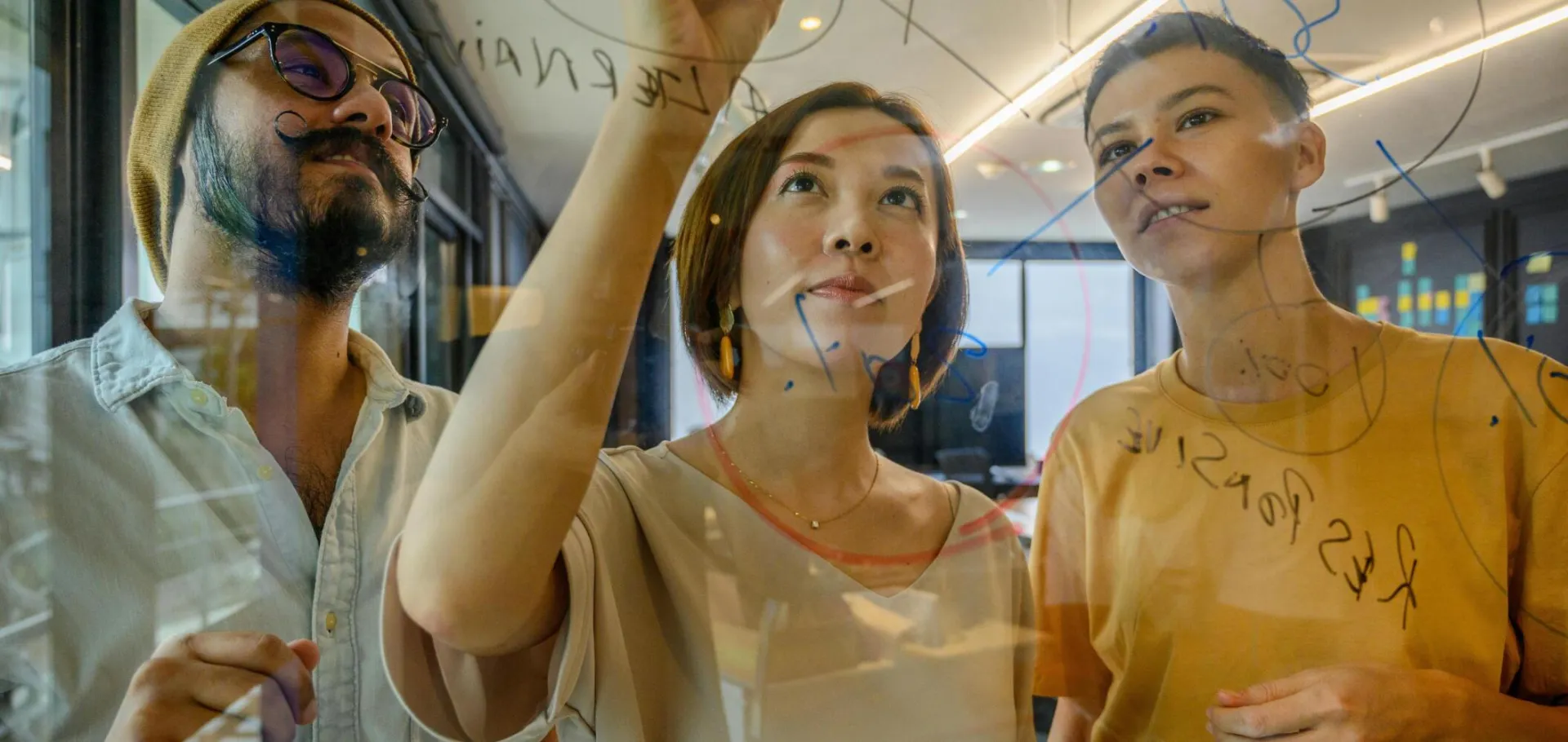 Group of diverse professionals collaborating on a glass board in a modern office setting.