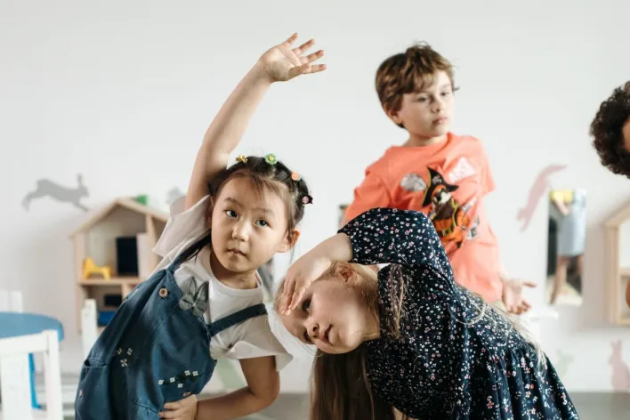 Kids performing stretching exercises indoors with playful energy.
