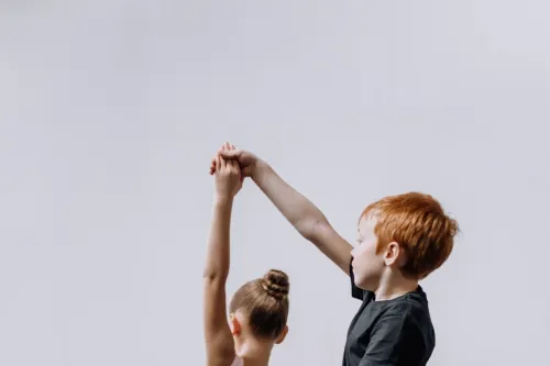 A young boy and girl practicing ballet dance in a studio, holding hands gracefully.