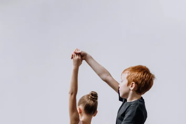 A young boy and girl practicing ballet dance in a studio, holding hands gracefully.