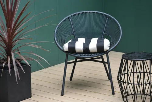 Stylish outdoor patio scene featuring a modern black chair with a striped cushion, a potted plant, and a wire stool.