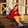 Young woman with a smartphone and coffee on wooden steps, enjoying the sunset.