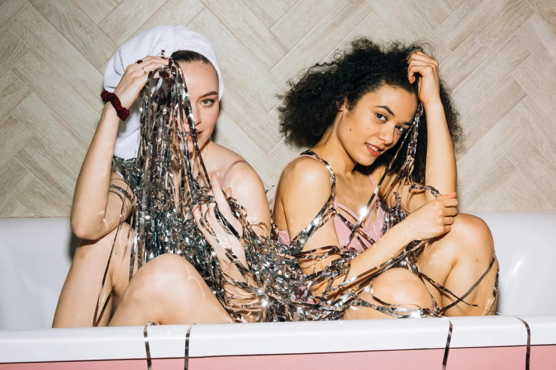 Two young women having a playful time in a bathtub with shiny streamers.