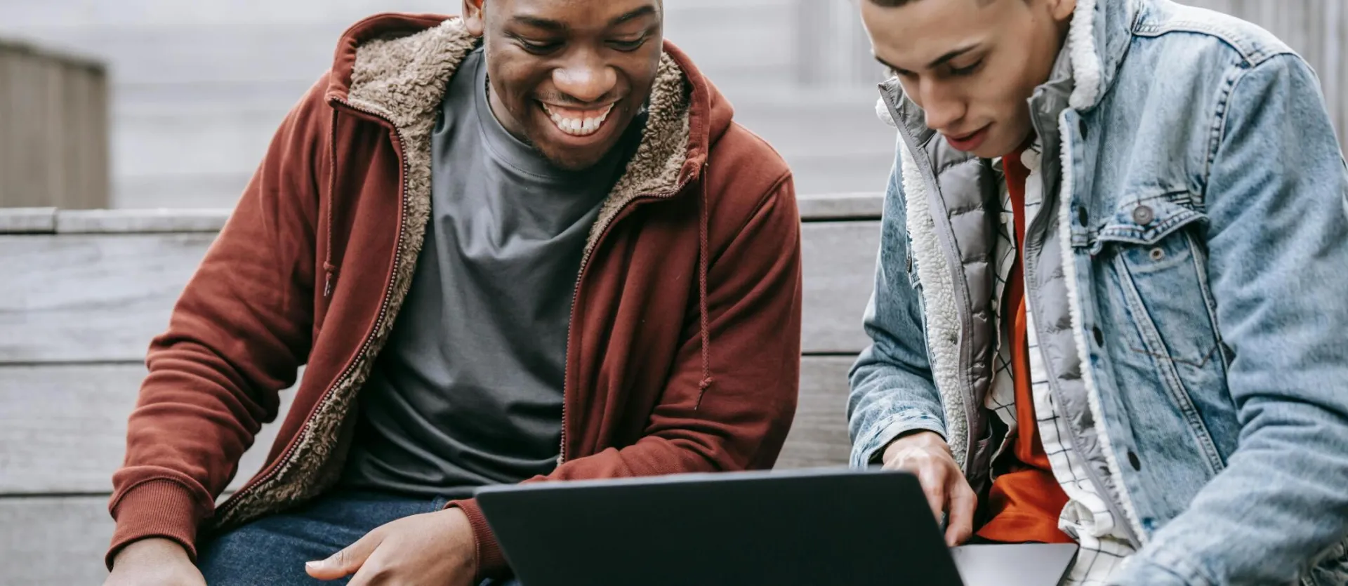 Crop content young multiracial male partners in casual outfit surfing internet on portable computer on urban staircase