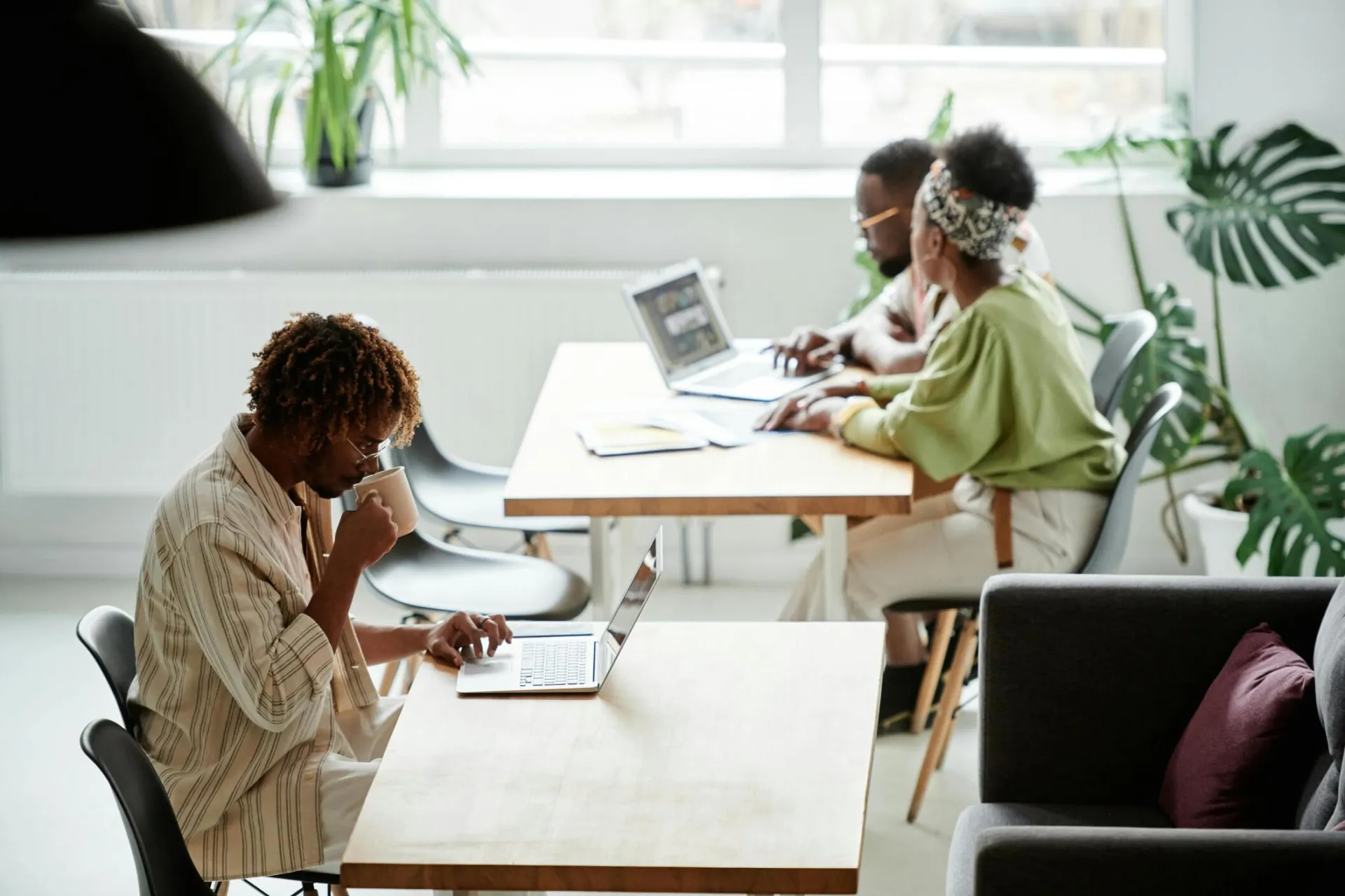 Diverse coworkers working in a modern office space with laptops and coffee, promoting teamwork and productivity.