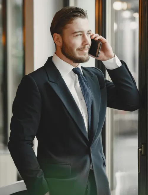 A businessman in a suit talks on the phone by a window, exuding confidence and professionalism.