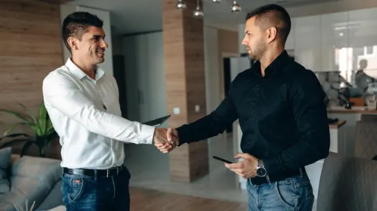 Two business professionals shaking hands in a modern office environment, symbolizing partnership.