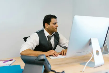 Professional man in office attire typing on computer at a modern desk.